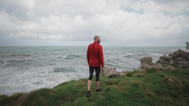 Runner in Red Sportswear Overlooking Stormy Sea After Workout, Contemplative Moment