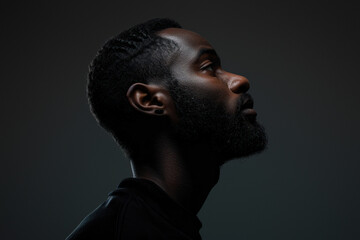 The image captures a side profile of an African man with a modern hairstyle against a dark background, giving it a moody feel