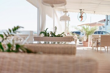 Wicker furniture tables in the open air are waiting for visitors. The interior of the restaurant in...