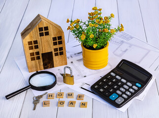 Home loan concept. Wooden house, calculator, house keys, magnifying glass, documents, design, flower in pot on white background.