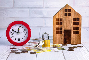Home loan concept. Wooden house, red alarm clock, house keys, euro bills and coins on a white...
