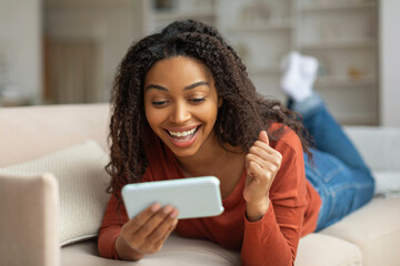 Black Woman Celebrates Victory on Smartphone in Living Room