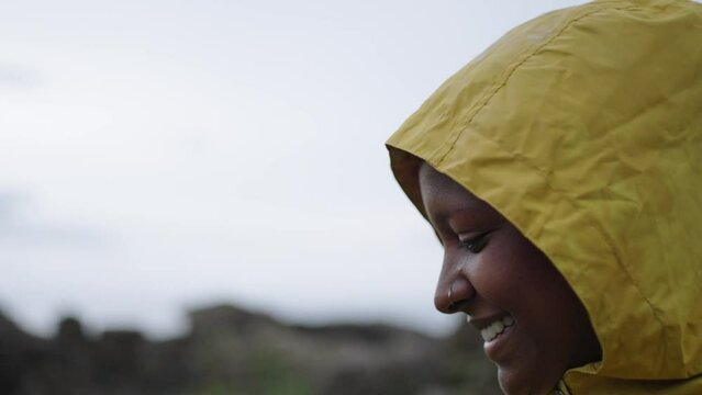 Young smiling African American woman in yellow raincoat in a natural landscape as explores the place. Happy woman feeling freedom in Nature enjoying her free time in vacations while it rains
