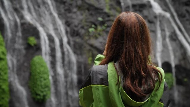 Woman photographing waterfall i the middle of the jungle. Bali, Indonesia. High quality FullHD slow motion footage.