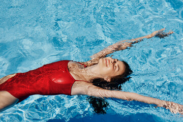 Happy woman swimming in pool in red swimsuit with loose long hair, skin protection with sunscreen, concept of relaxing on vacation. - obrazy, fototapety, plakaty