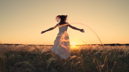 Free girl runs happily through meadow in grass in rays of sunset. Concept of female dreams,...