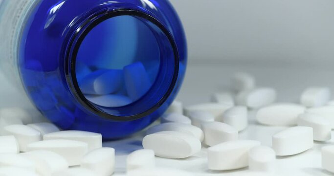 Big white pills scattered on table. Overdose. Open blue container for nutritional supplements lies on table. In reality these are biologically active sulfur pills in dosage of 1500 mg, MSM for joints