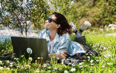 Young woman lying on a green summer lawn using a laptop