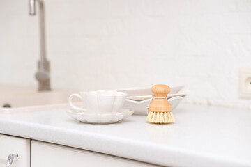 Side view of bamboo dishwashing brushes near sink and plates on table in kitchen. Washing dishes. Home comfort. Eco-friendly kitchenware. Household equipment. Concept of cleanliness