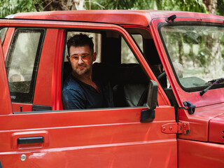 Attractive man and a red SUV against a background of palm trees. Sunny, clear day. Closeup, outdoor. Vacation and travel concept