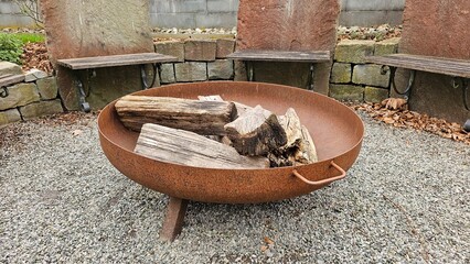 A large fire pit with wood in it sits in front of a stone wall