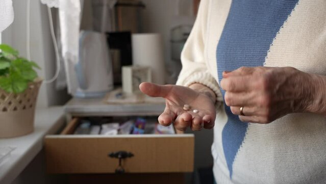 Close up of old woman hands holding medicine pills and trying to remember how much she took of them. Alzheimer, elderly woman counting her drugs.