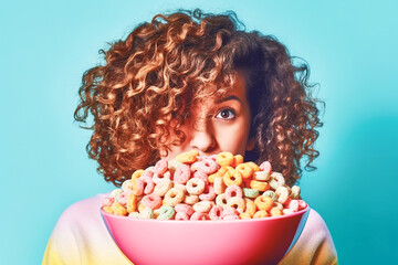 Funny young woman with red curly hair peeping from behind a bowl with colorful cheerios cereal....