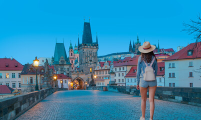 A beautiful woman in a white hat and mini jean shorts walks towards the old town -  View of Charles Bridge and Lesser Bridge Tower in Prague, Czech Republic