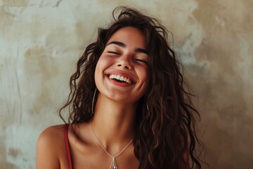 Joyful young woman with curly hair laughing against a textured beige background.