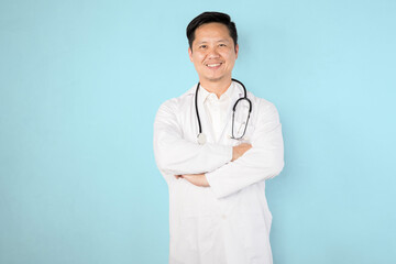 A smiling doctor stands with his arms crossed in front of a blue wall. Concept of professionalism...