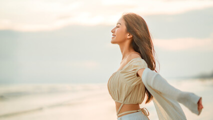 Happy young asian woman with freedom on the sea beach at golden sunset, Female tourist on seaside summer vacation.