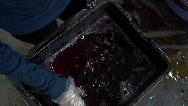 Slow motion footage of participants learning to dye traditional batik cloth by dipping dye in a basin and boiling water. Beginners learn the process of dyeing batik cloth in the traditional way