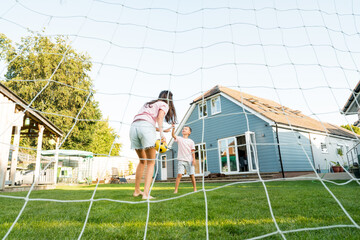 Young mother and son giving five during soccer game in the garden. Happy family playing football, having fun together. Fun Playing Games in Backyard Lawn on Sunny Summer Day. Motherhood, childhood.