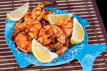 large barbeued black tiger shrimp on a blue fish shaped plate with lemon wedges
