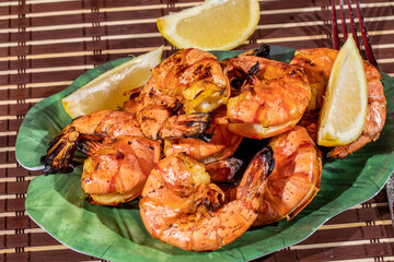 a meal of large barbecued black tiger shrimp on a green leaf shaped plate with lemon wedges