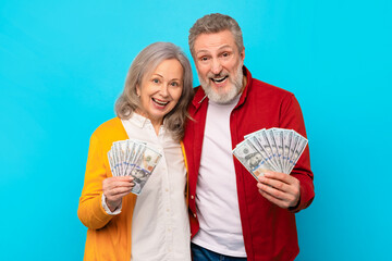 senior man and woman holding money cash against blue backdrop