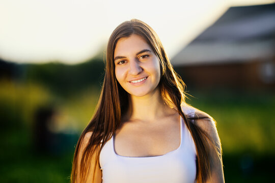 Portrait of young Caucasian woman against blurred rural background in light of setting sun in summer.