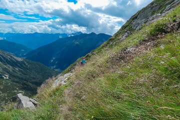 Hiker woman disappearing behind high grass of alpine meadow. Scenic view of majestic mountain peaks...