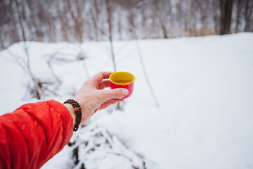 A mug of delicious fragrant tea in a man's hand on the background of snow in winter in the forest,...