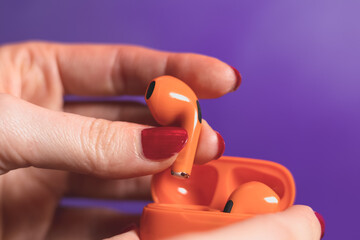 Woman is taking out of the box Orange Wireless Bluetooth Earphones. Modern Stereo Earplugs, Sports Headset.