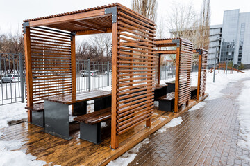 Wooden pergola with table and benches on snowcovered floor