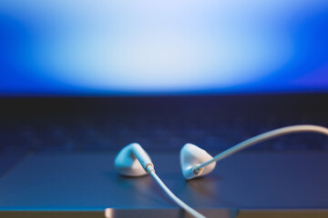 White Earphones lying on the laptop. Modern music concept. Audio technology. Close up photo. - obrazy, fototapety, plakaty