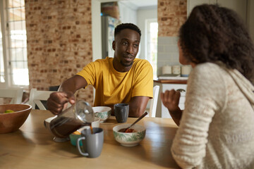 Young African man pouring coffee for his wife during breakfast