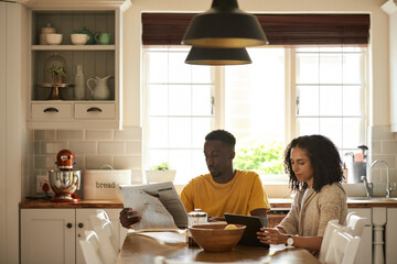 Young multiethnic couple catching on news during breakfast in their kitchen