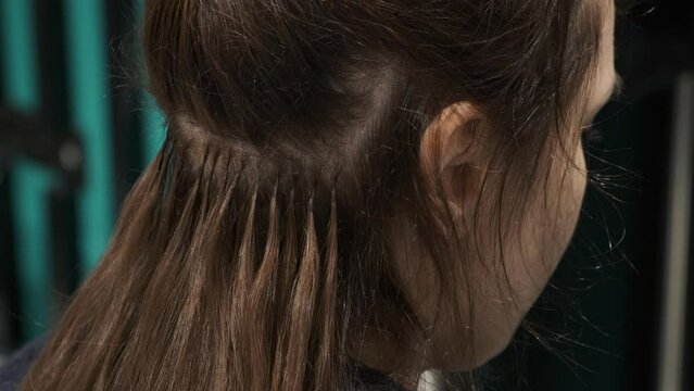Hair extension with capsules and strands of grown brunette hair in beauty salon, Fusion hair extension with keratin, beauty procedure, increase hair volume. Close up