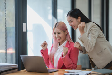 Obraz premium Two asian businesswomen are smiling and celebrating on a laptop