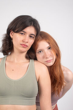 Two young women posing together, one with short hair and the other with long red hair, against a white background.