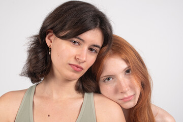 Two young women posing closely with serious expressions, isolated on a white background.