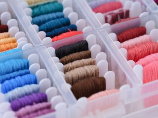 Plastic sorting box full of bobbins with different color embroidery threads. Close-up