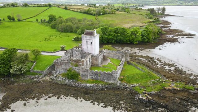 A wide drone shot of an old Irish castle, in the green fields along the coast. Doe Castle, Co. Donegal, Ireland