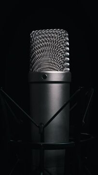 Vertical studio microphone rotates on a black background close-up. Condenser microphone grid surface spinning around. Concept recording studio, voice, broadcast.
