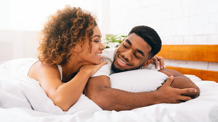 Loving black couple relaxing in bed at home