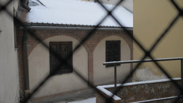 Snow falls behind the bars of an old stone building in the winter city in Europe.