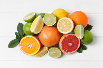 Different fresh citrus fruits and leaves on white wooden table, flat lay