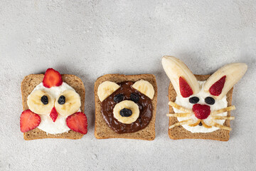 Sweet toasts for kids in shape of chick, bear and rabbit, with strawberries, banana, cream cheese, chocolate and coconut flakes on gray background, Top view