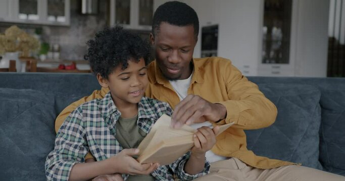 Happy African American people adult man and child reading book spending time together at home. Intelligent hobby and childhood concept.