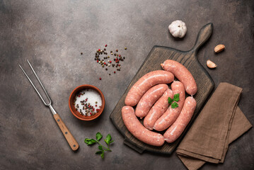 Raw homemade sausages on a wooden cutting board with spices and a meat fork, dark rustic...