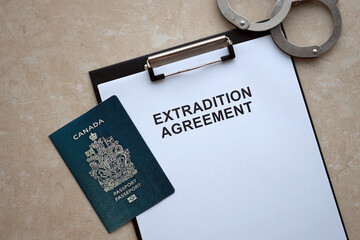 Passport of Canada and Extradition Agreement with handcuffs on table close up