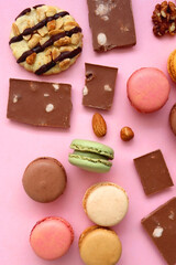 Pastel macarons, almond chocolate, peanut butter cookies and various nuts on bright pink background. Top view.