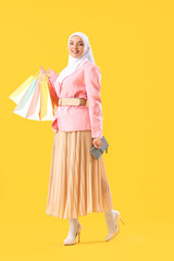 Beautiful young Muslim woman with shopping bags and purse on orange background - obrazy, fototapety, plakaty